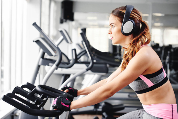 Attractive young woman working out on exercise bike in gym  - Photo, Image