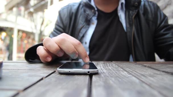 Jonge man met zijn smartphone in een café. Close-up van handen - Video