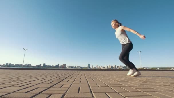 Young caucasian woman performs acrobatic flip on the asphalt on background cityscape - Video