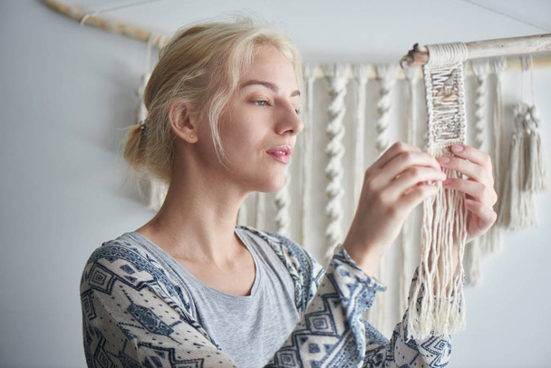 blonde woman weaving element of macrame decoration, female hobby concept  - Foto, afbeelding