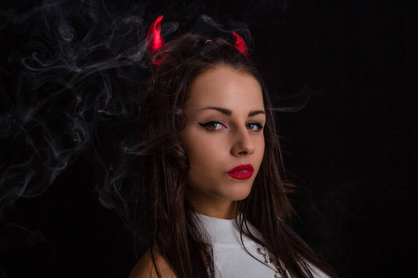 женщина с дьявольскими рогами и сигаретным дымом позирует на черном фоне
 - Фото, изображение