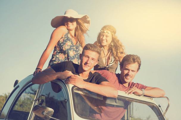 Ομάδα από χαρούμενους ανθρώπους σε ένα αυτοκίνητο το ηλιοβασίλεμα το καλοκαίρι, έτοιμοι για ένα οδικό ταξίδι. - Φωτογραφία, εικόνα