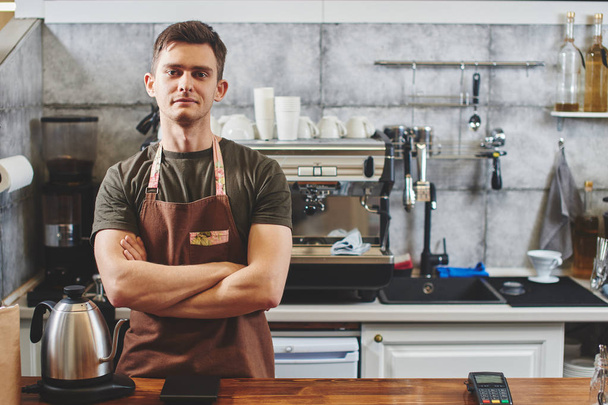 male waiter with crossed arms standing at workplace in coffee shop - Photo, image