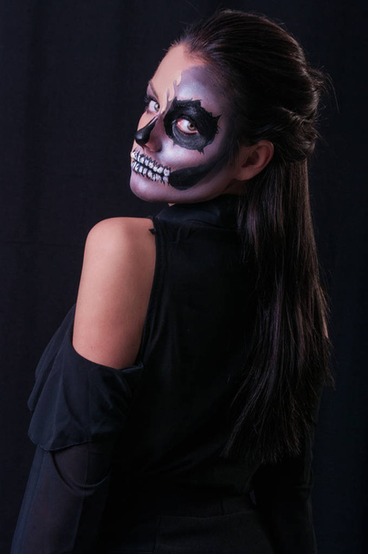 Studioporträt einer brünetten Frau mit beängstigender Farbe im Gesicht, die auf schwarzem Hintergrund posiert  - Foto, Bild