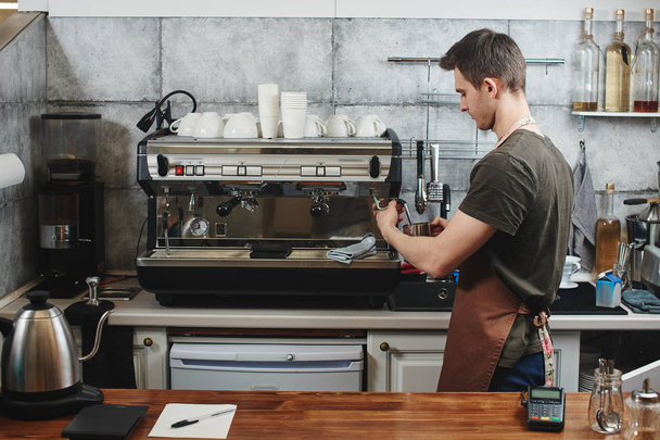 handsome barista in apron making cappuccino with coffee machine  - Фото, зображення