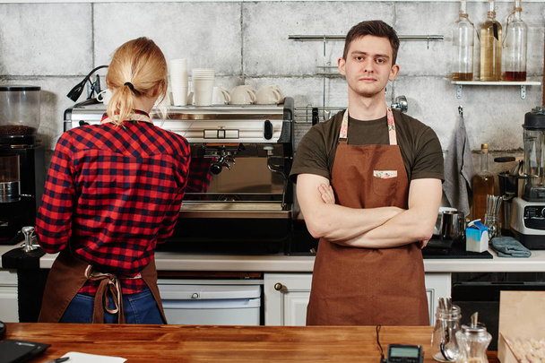 male barista standing with crossed arms near female waitress at workplace  - Foto, imagen