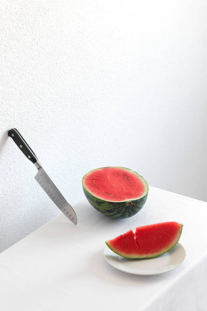 Half of watermelon and knife on a white table with copy space - Фото, изображение