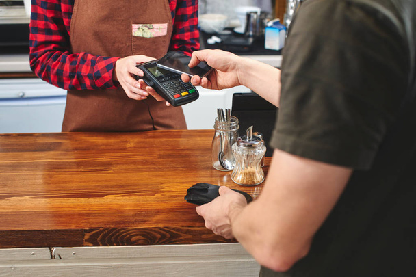 male customer paying for coffee barista woman with smartphone - Foto, afbeelding