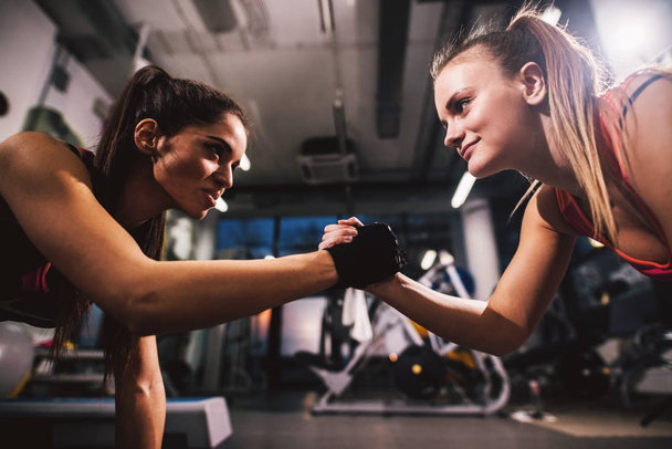 twee jonge aantrekkelijke vrouwen doet push ups in sportschool en hand in hand - Foto, afbeelding