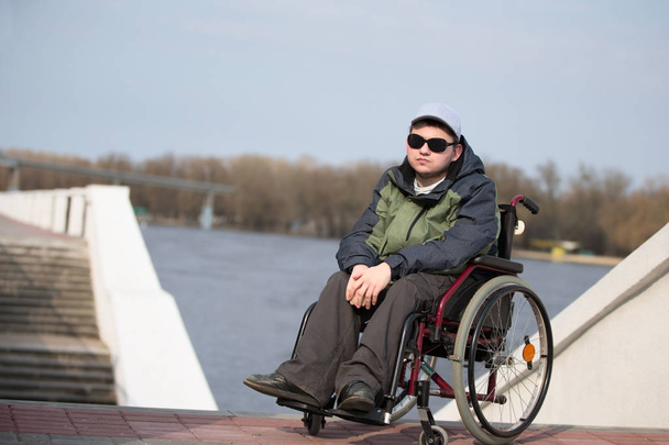 Ένας άντρας που φοράει γυαλιά ηλίου σε αναπηρικό καροτσάκι για βόλτα. - Φωτογραφία, εικόνα