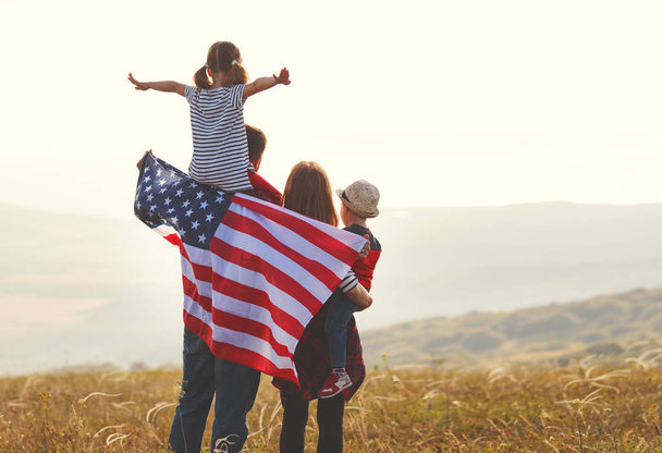 onnellinen perhe Amerikan Yhdysvaltojen lipun kanssa auringonlaskun aikaan ulkona
 - Valokuva, kuva