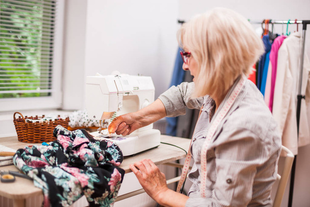 Volwassen vrouw is naaien in haar atelier. - Foto, afbeelding