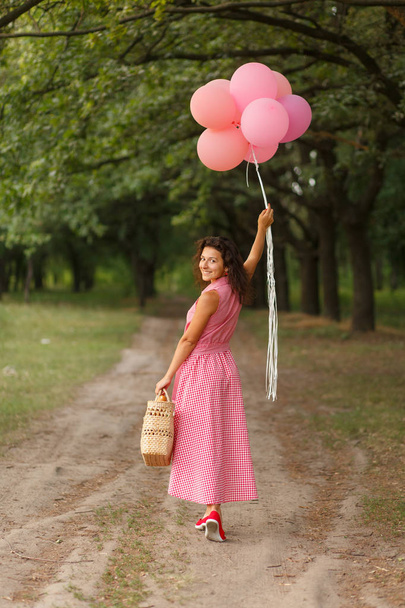 Kobieta w różowej sukience różowy balony i Wiklinowy kosz w zielonym parku Niedziela - Zdjęcie, obraz
