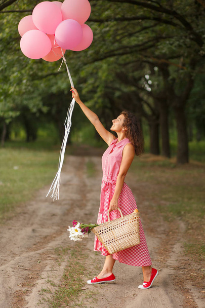 Kobieta w różowej sukience różowy balony i Wiklinowy kosz w zielonym parku Niedziela - Zdjęcie, obraz