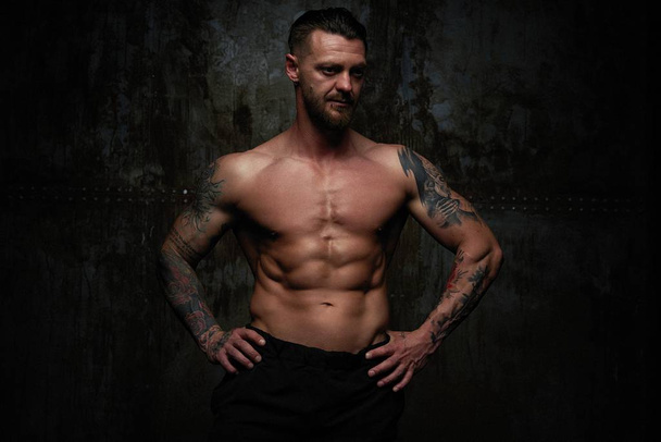 Shirtless muscled young man posing against grunge wall background  - Zdjęcie, obraz
