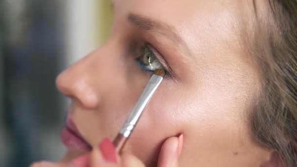 Side view of a models face. Make up artist applying eyeshadows under the lower eyelid with brush. Blue eyeliner. Make up process - Metraje, vídeo