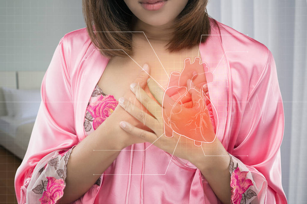 Ασιατικές γυναίκα σε ροζ σατέν νυχτικά πόνους στο στήθος της το βράδυ. Οξύς πόνος πιθανή καρδιακή προσβολή. Καρδιακή νόσο ή στενοχώρια - Φωτογραφία, εικόνα
