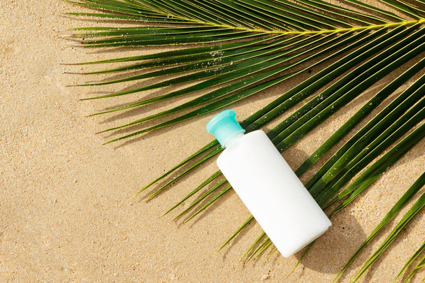 Bottle of sun protection lotion and palm leaf on the beach - Fotoğraf, Görsel