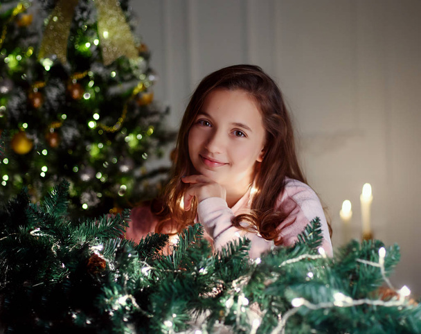 Young beautiful girl in the New Year stands by the fireplace - Фото, зображення