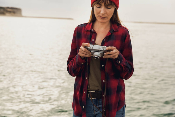 Woman in red and black checkered shirt standing with camera at lake. - Foto, immagini