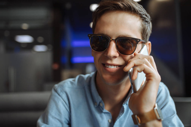 Happy young man in glasses, emotionally talking on the phone, sitting in a cafe, - Photo, Image