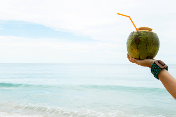 Female hand with a coconut cocktail on beach - 写真・画像