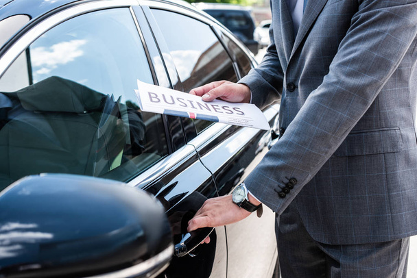 cropped shot of businessman with newspaper opening car door on street - Photo, Image
