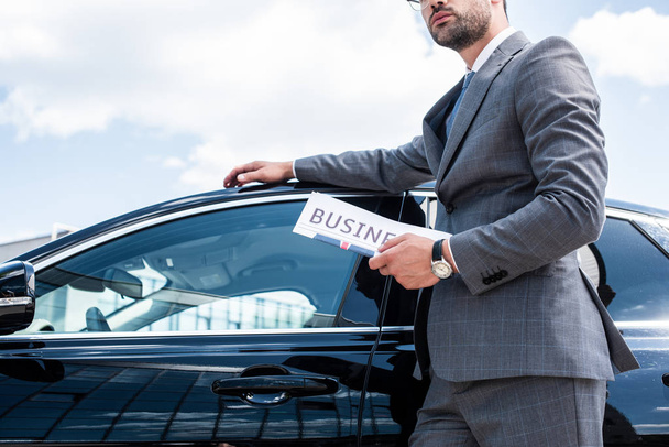 partial view of businessman with newspaper standing at car on street - Foto, Imagen