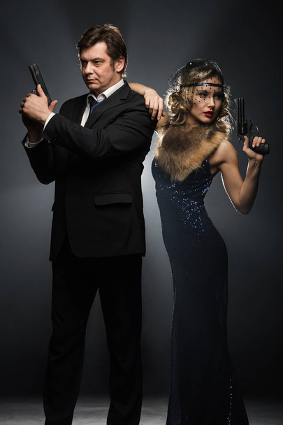 A pair of gangsters, a man and woman with guns on black background with smoke - Foto, Imagen