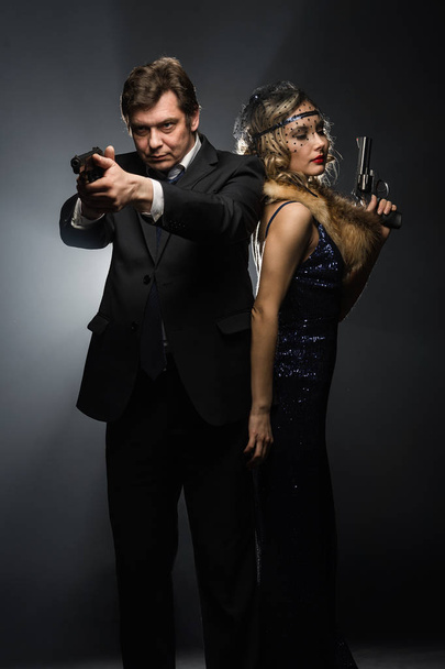 A pair of gangsters, a man and woman with guns on black background with smoke - 写真・画像