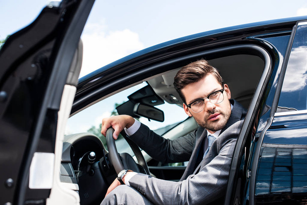pensive businessman in eyeglasses looking away while sitting in car - 写真・画像