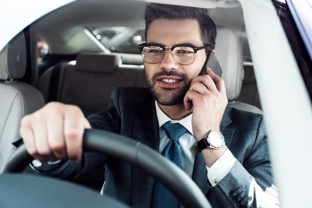 portrait of smiling businessman talking on smartphone while driving car - Photo, Image