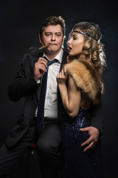 Un par de gángsteres glamour fumador, un hombre y una mujer con cigarrillos sobre fondo negro con humo
 - Foto, imagen