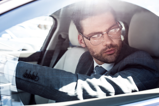 side view of businessman in eyeglasses looking away while driving car - Photo, Image
