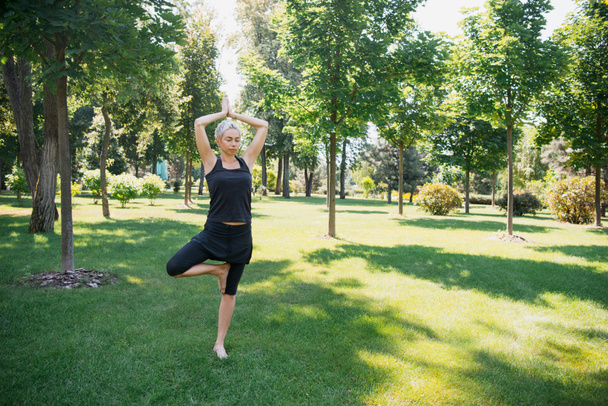 Nainen harjoitellaan jooga Tree poseeraa (Vrksasana) nurmikolla puistossa
 - Valokuva, kuva