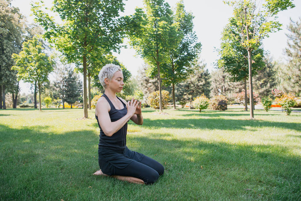 woman practicing yoga and making gesture with hands on grass in park - Photo, Image