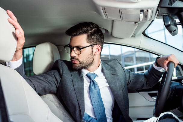 businessman in eyeglasses looking away while driving car - 写真・画像