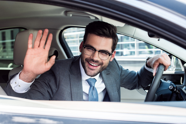 vue latérale de l'homme d'affaires joyeux saluant quelqu'un tout en conduisant une voiture
 - Photo, image