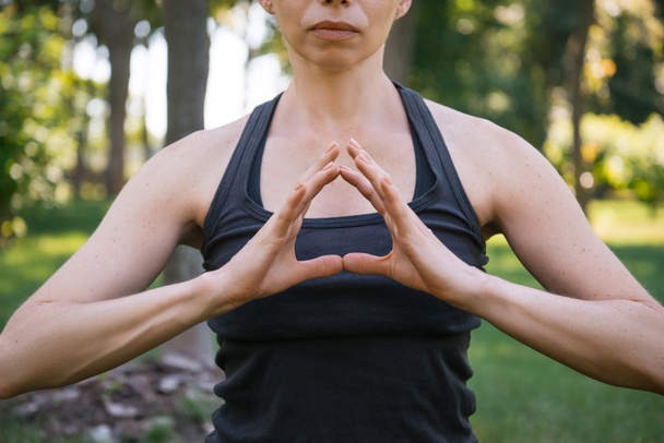 обрезанный образ женщины медитирующей и делающей жест руками в парке
 - Фото, изображение