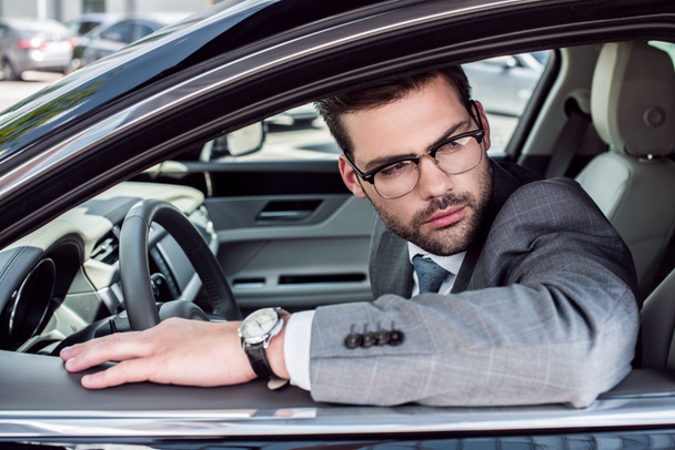 side view of pensive businessman in eyeglasses looking away while driving car - Foto, Imagen