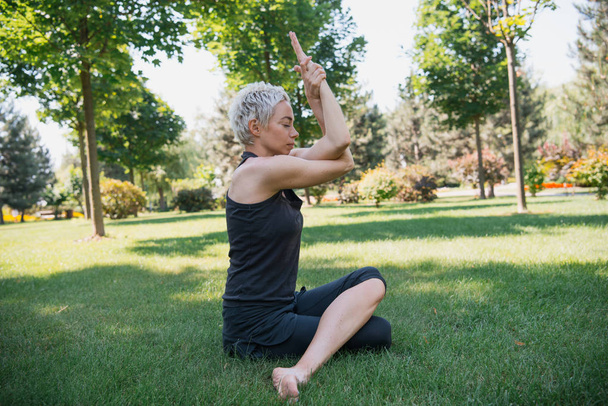 boční pohled na ženy cvičí jógu a sedí na trávě v parku - Fotografie, Obrázek