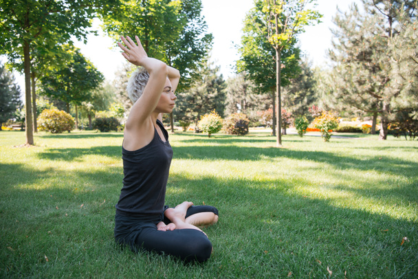 vista laterale della donna che pratica yoga in posa loto con le mani sollevate facendo gesto namaste sull'erba nel parco
 - Foto, immagini