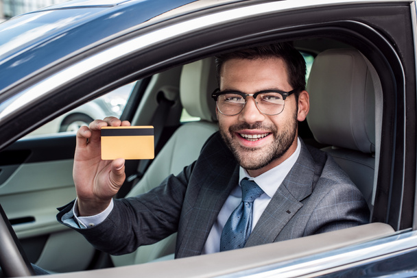 retrato de un hombre de negocios sonriente mostrando la tarjeta de crédito en la mano mientras está sentado en el coche
 - Foto, Imagen