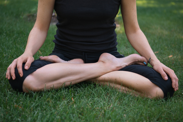 обрезанный образ женщины, практикующей йогу в позе лотоса на траве в парке
 - Фото, изображение