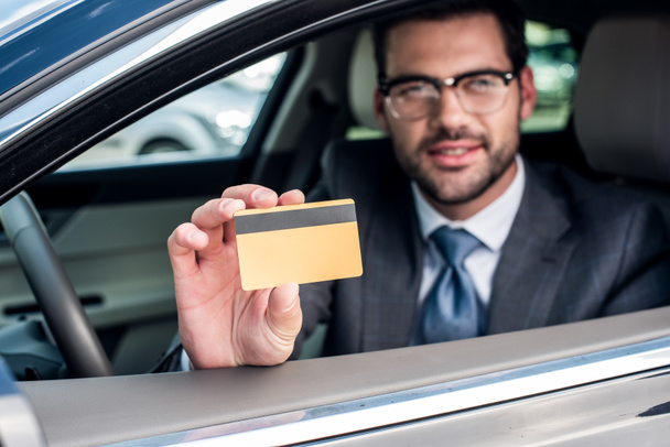 enfoque selectivo de hombre de negocios mostrando la tarjeta de crédito en la mano mientras está sentado en el coche
 - Foto, Imagen