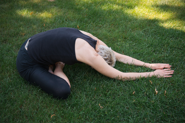 side view of woman practicing yoga in Wide Child pose (Balasana) on grass in park - 写真・画像