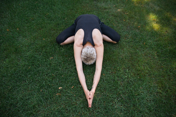 high angle view of woman practicing yoga in Wide Child pose (Balasana) on grass in park - Photo, Image