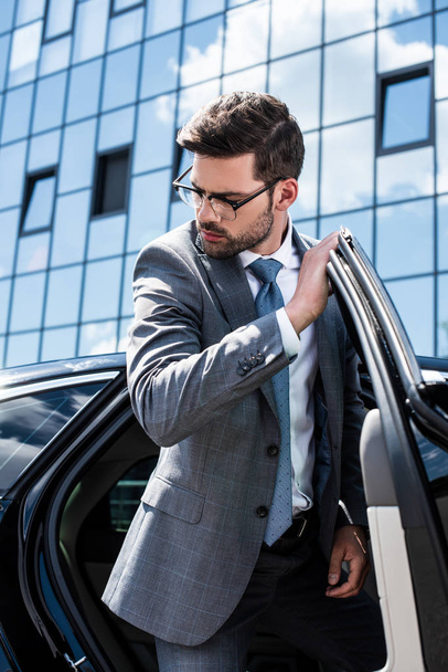 young businessman in suit and eyeglasses walking out car - Foto, afbeelding