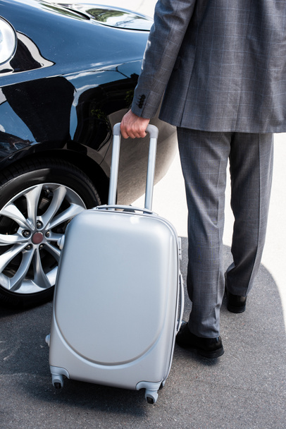  cropped image of businessman carrying wheeled bag near car at street  - Zdjęcie, obraz