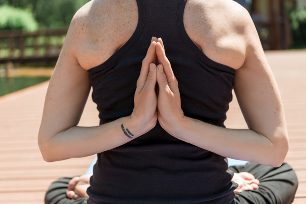 abgeschnittenes Bild einer Frau, die Yoga in Lotus-Pose praktiziert und Hände in Namaste-Geste im Park - Foto, Bild
